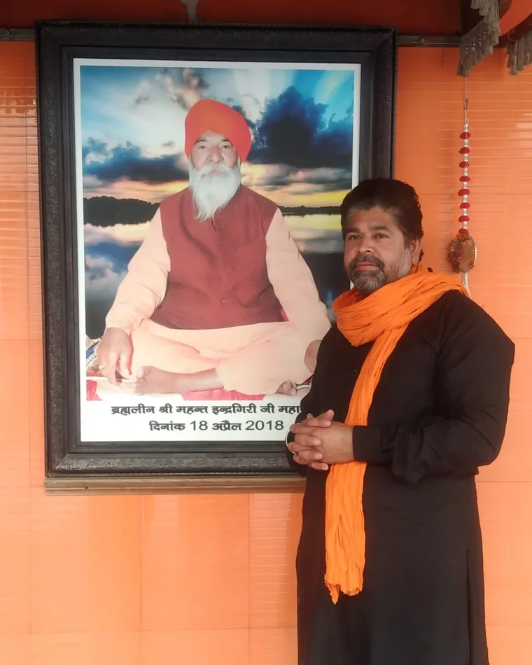 The founder of Gau Vansh Sewa Dham standing beside a framed portrait of the late Mahant.