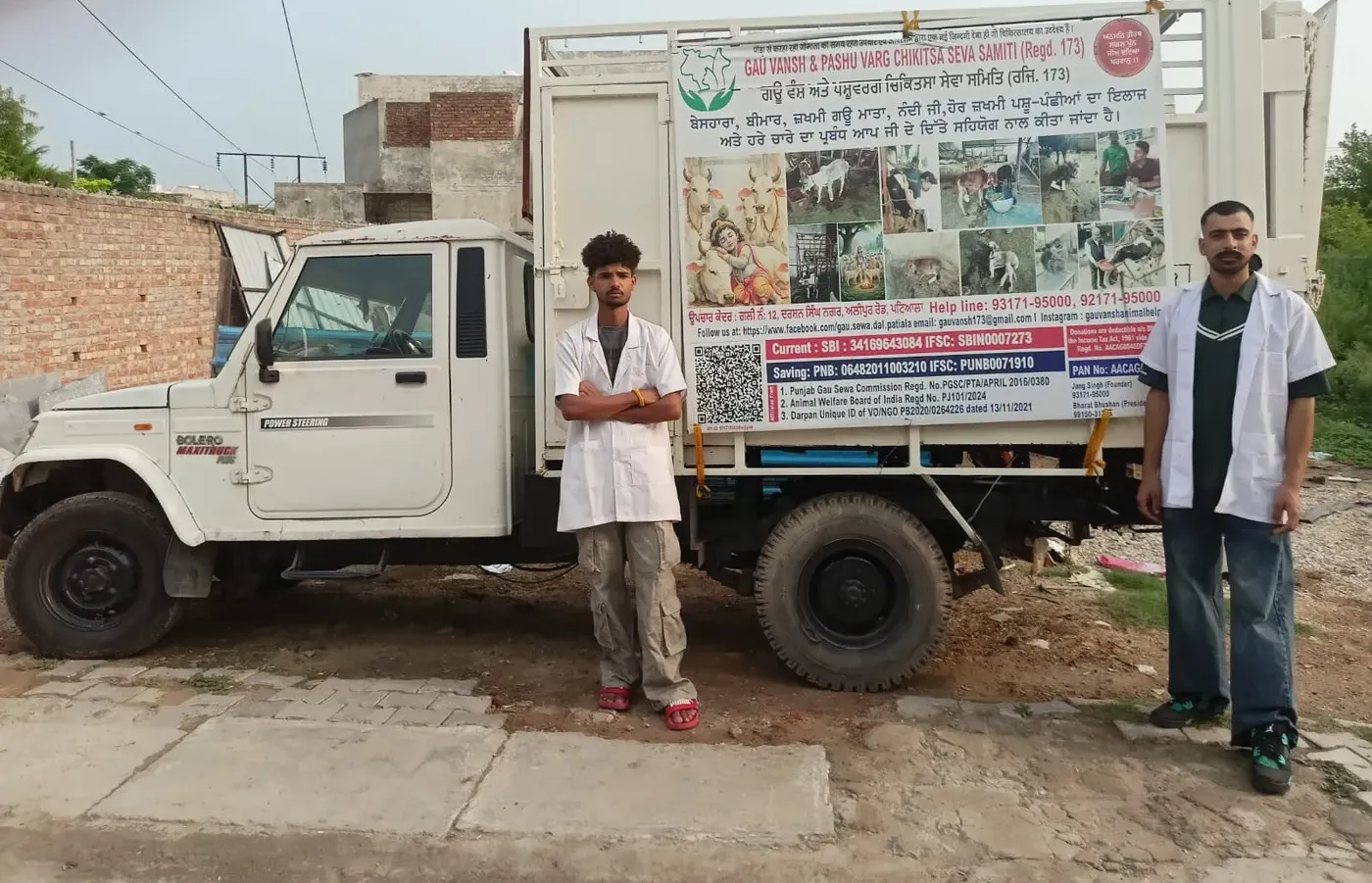 Two staff in white coats standing beside the gaushala's own rescue ambulance truck.