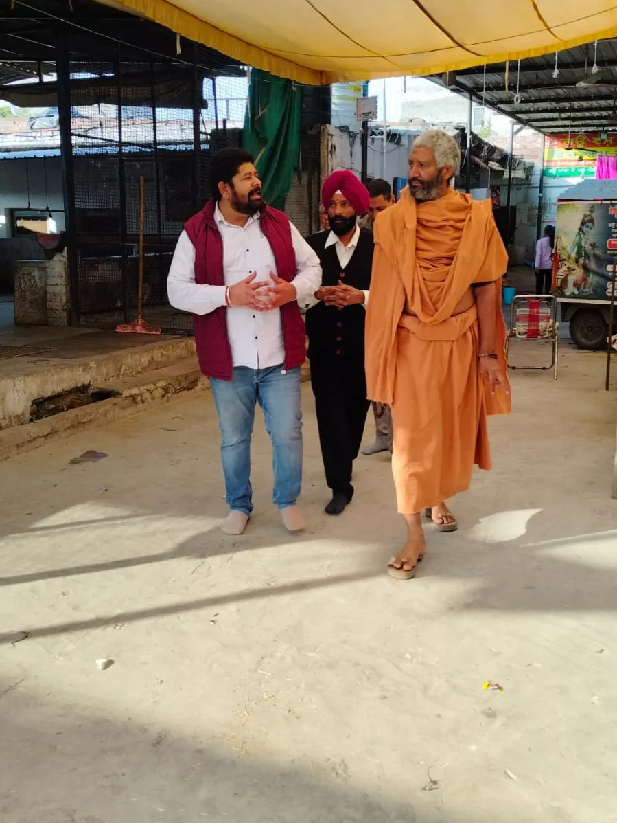 A visiting mahant walking through the gaushala with supporters, beside the donation seva vehicle.